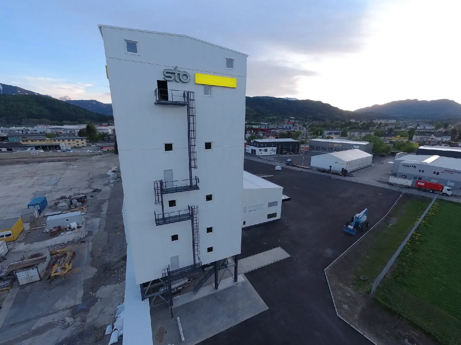 Turm des Sto-Werks in Villach bei Tag: oben der Schriftzug „sto“ und daneben der gelbe Kasten an der hellen Fassade