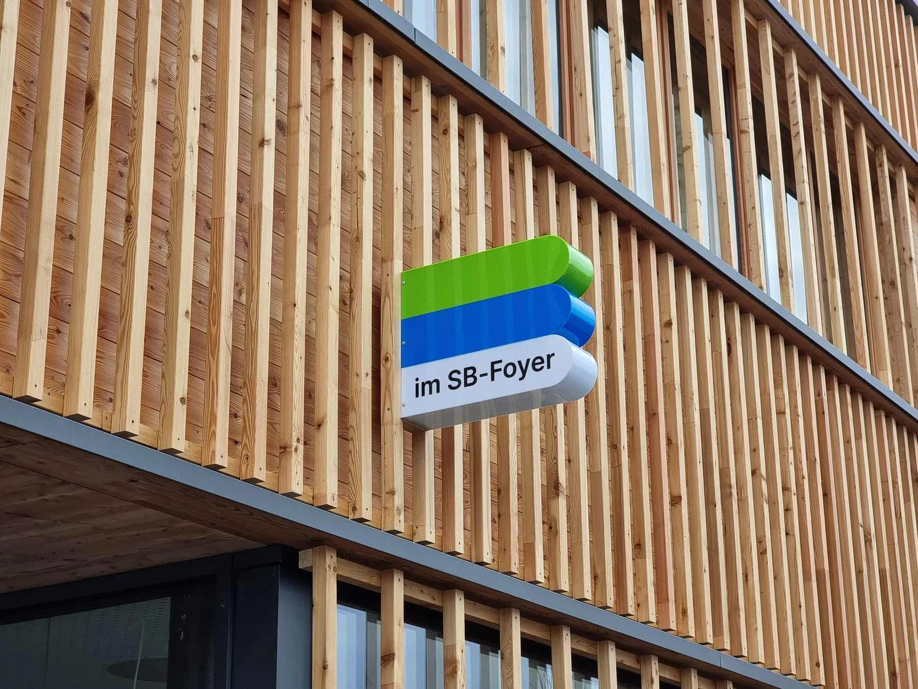Zusatzschild „im SB-Foyer“ an der Lattenfassade