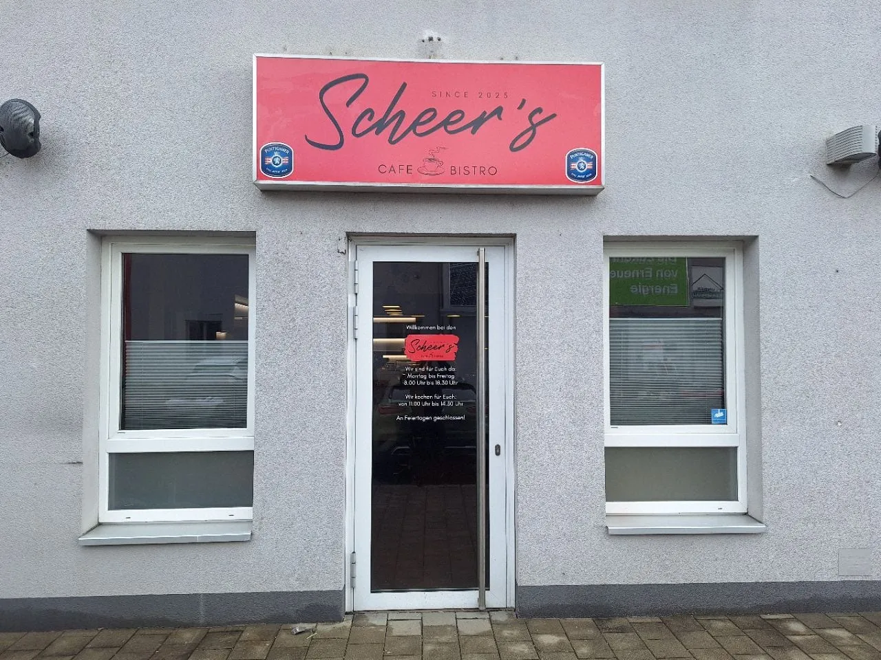 Roter Leuchtkasten mit Puntigamer-Logos über dem Eingang eines Cafés, dazu Öffnungszeiten auf der Glastür