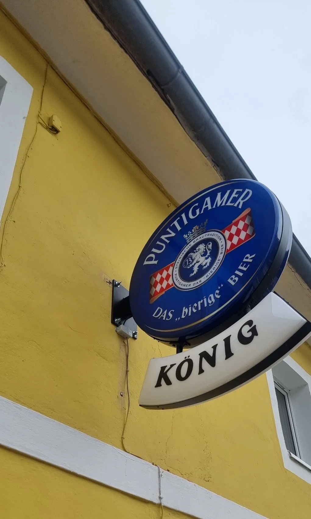Fertig montierter Puntigamer-Ausleger mit Namensschild an der gelben Fassade