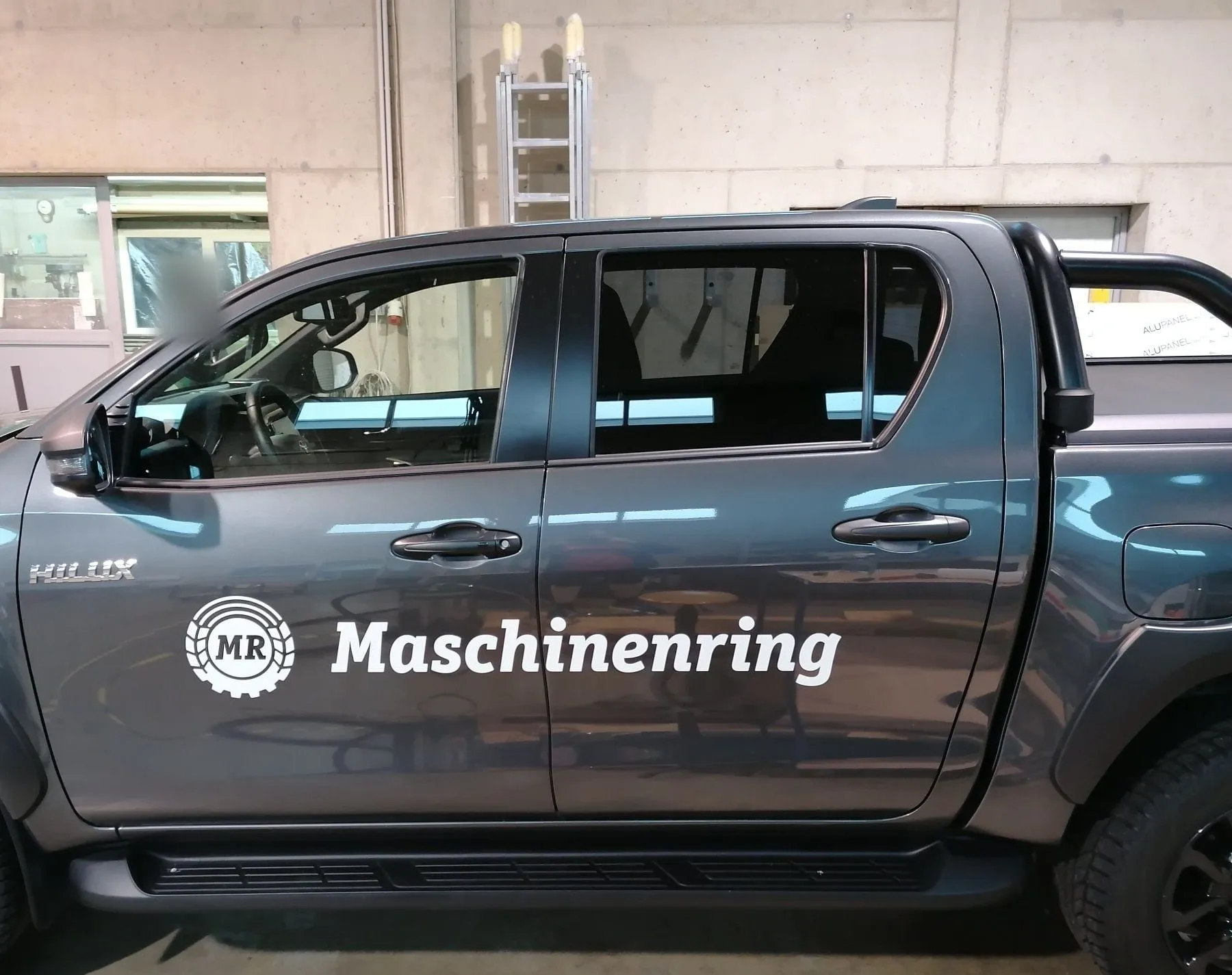 Grauer Toyota Hilux mit Maschinenring-Logo und Schriftzug an den Türen, Seitenansicht in unserer Halle