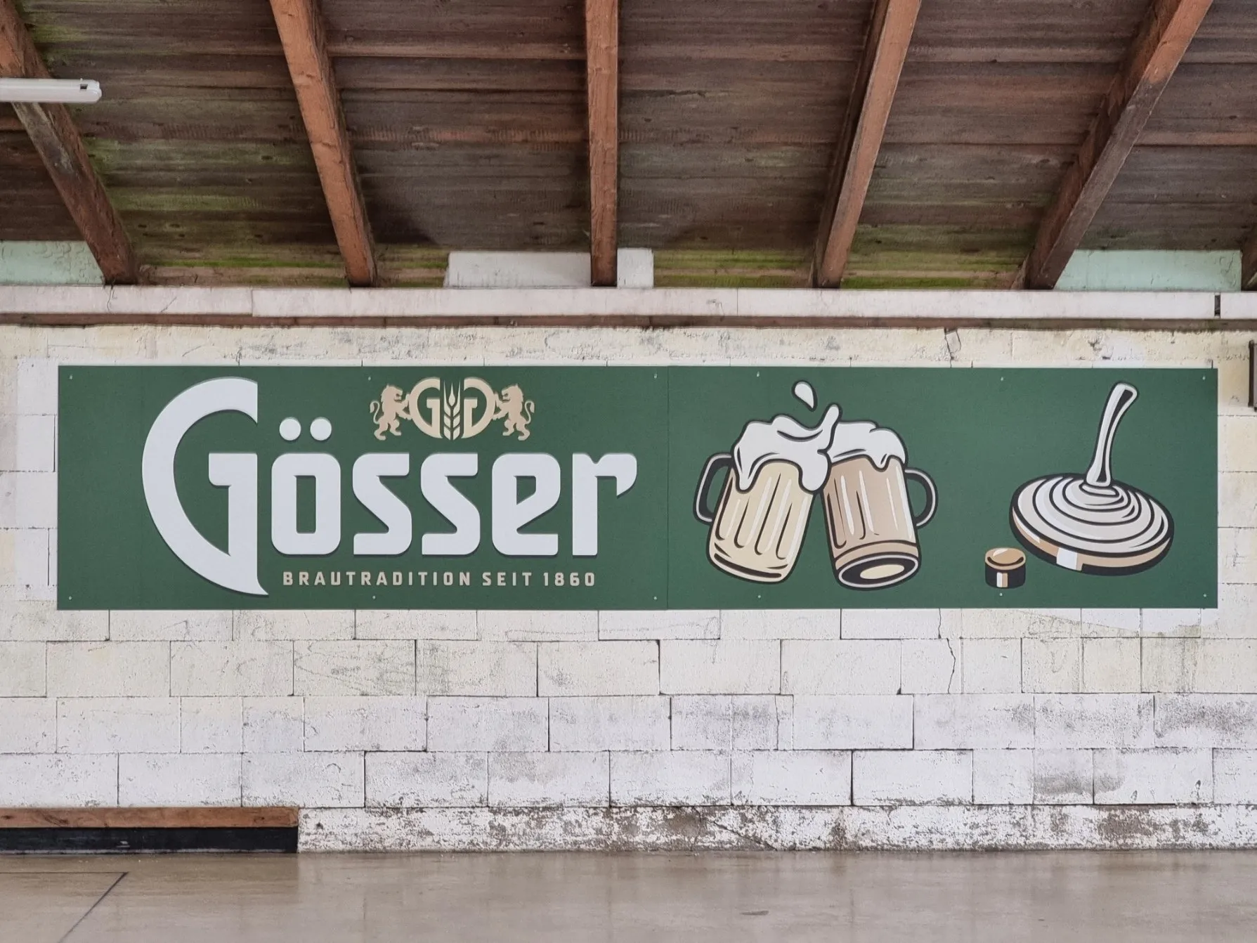 Gösser-Werbetafel „Brautradition seit 1860“ mit Bierkrügen und Eisstock in einer Stockschützenhalle