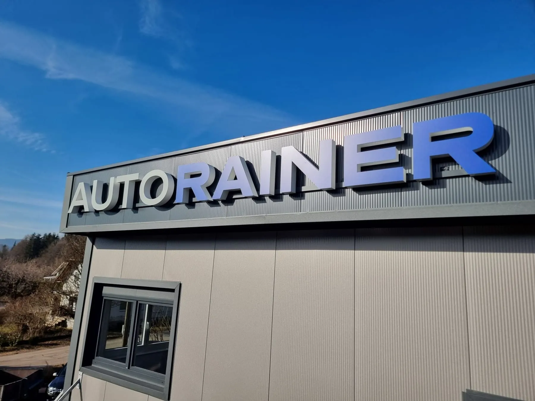 3D-Schriftzug AUTO RAINER an der Hallenfassade