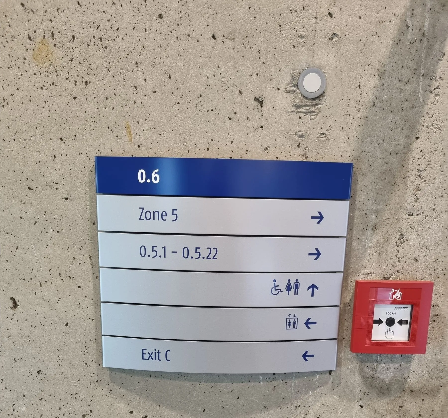 Modulares Wegweiserschild aus Aluminium mit Zone, Raumnummern, WC, Lift und Ausgang auf Sichtbeton