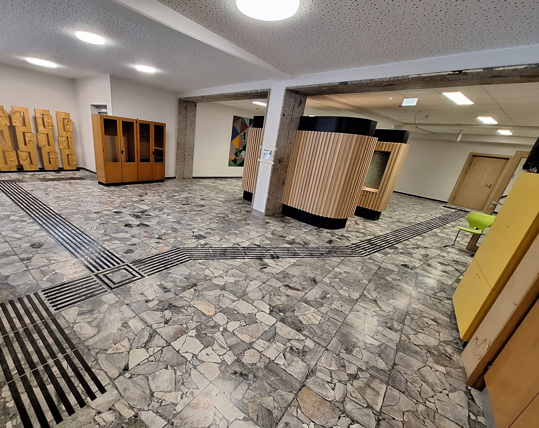 Schulaula mit taktilem Bodenleitsystem aus schwarzen Leitstreifen und Aufmerksamkeitsfeld auf Marmorboden