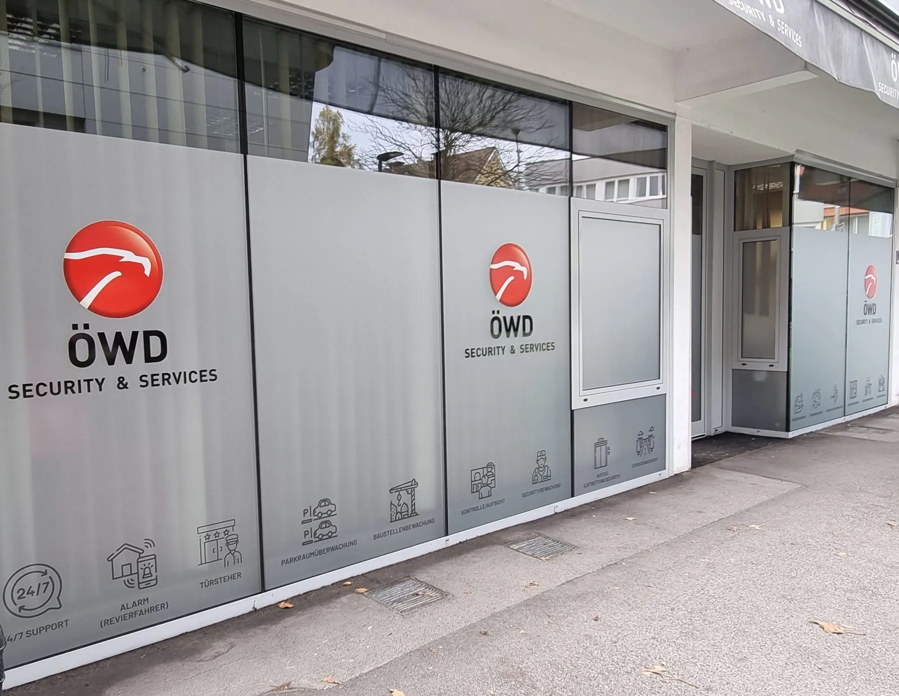 Schaufensterfront mit bedruckter Milchglasfolie, Logos und Piktogrammen der Leistungen eines Sicherheitsdienstes