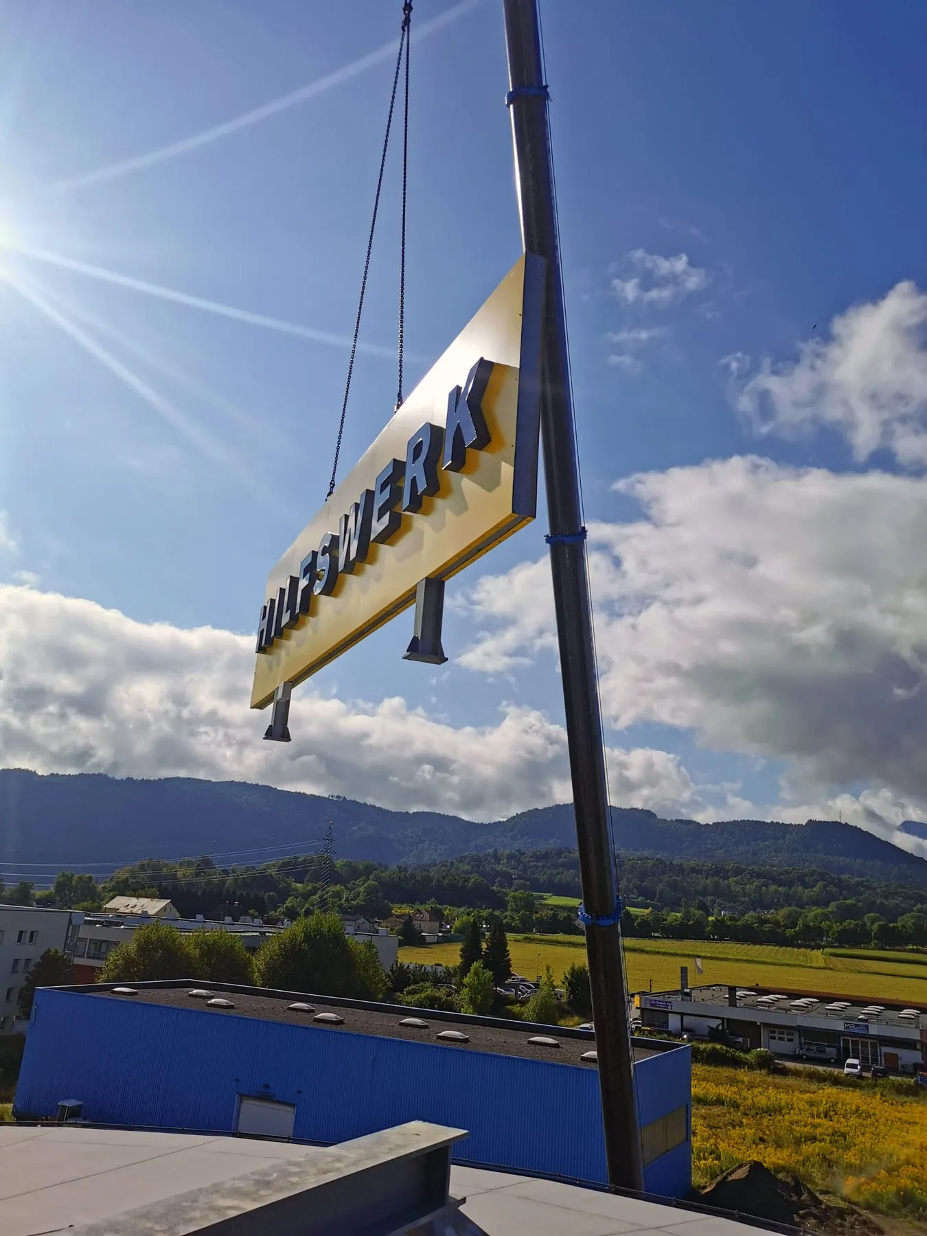 Ein Leuchtschild mit dem Schriftzug „Hilfswerk“ hängt am Kranhaken über dem Dach
