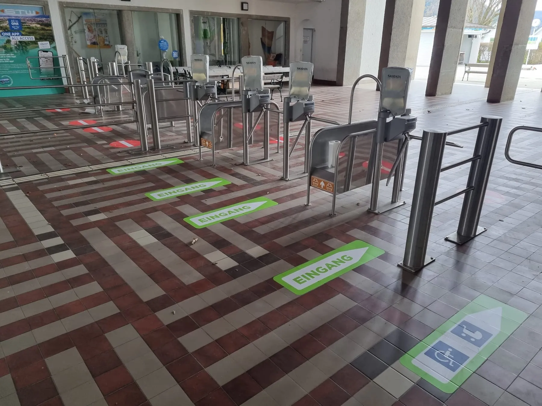 Grüne Bodenpfeile „Eingang“ und ein Pfeil für Rollstuhl und Kinderwagen an den Drehkreuzen des Strandbads Klagenfurt
